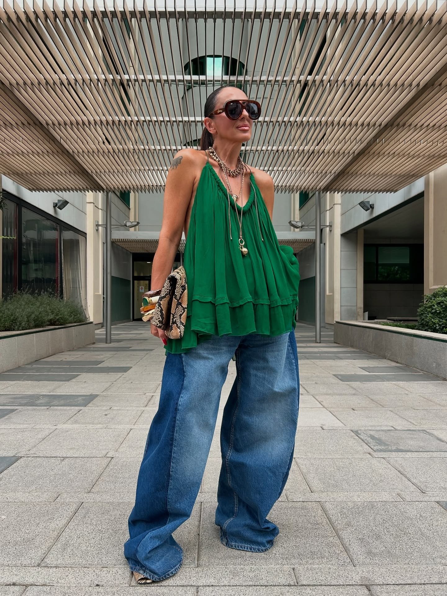 Look para sair à noite com blusa verde fluida de alças finas, jeans wide leg bicolor e acessórios dourados que expressam