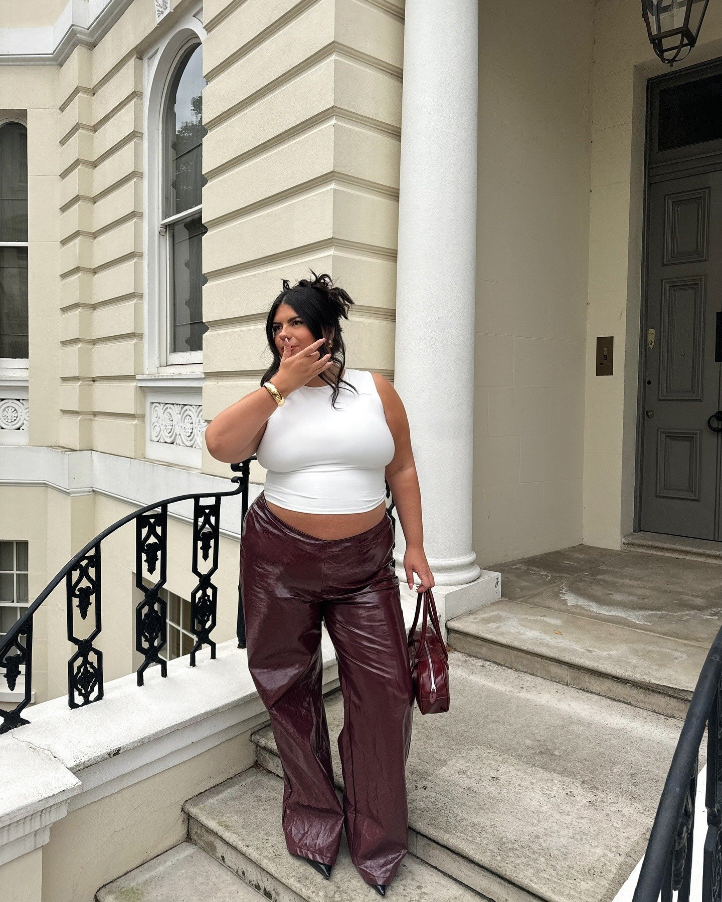 Modelo posa pensativa com cropped branco justo e calça vinho de material brilhante, criando looks para sair à noite modernos