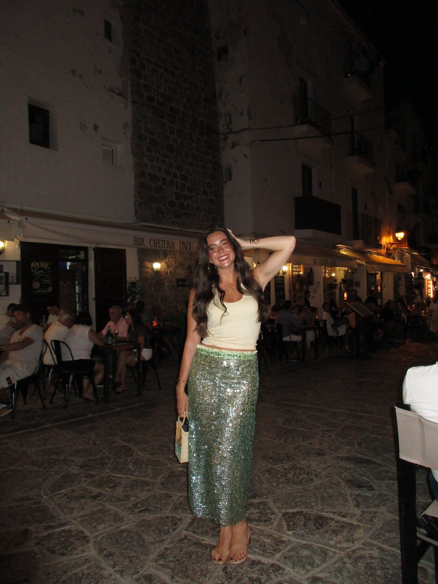 Look para sair à noite com saia midi verde brilhante de paetês, regata off-white e postura descontraída e alegre.