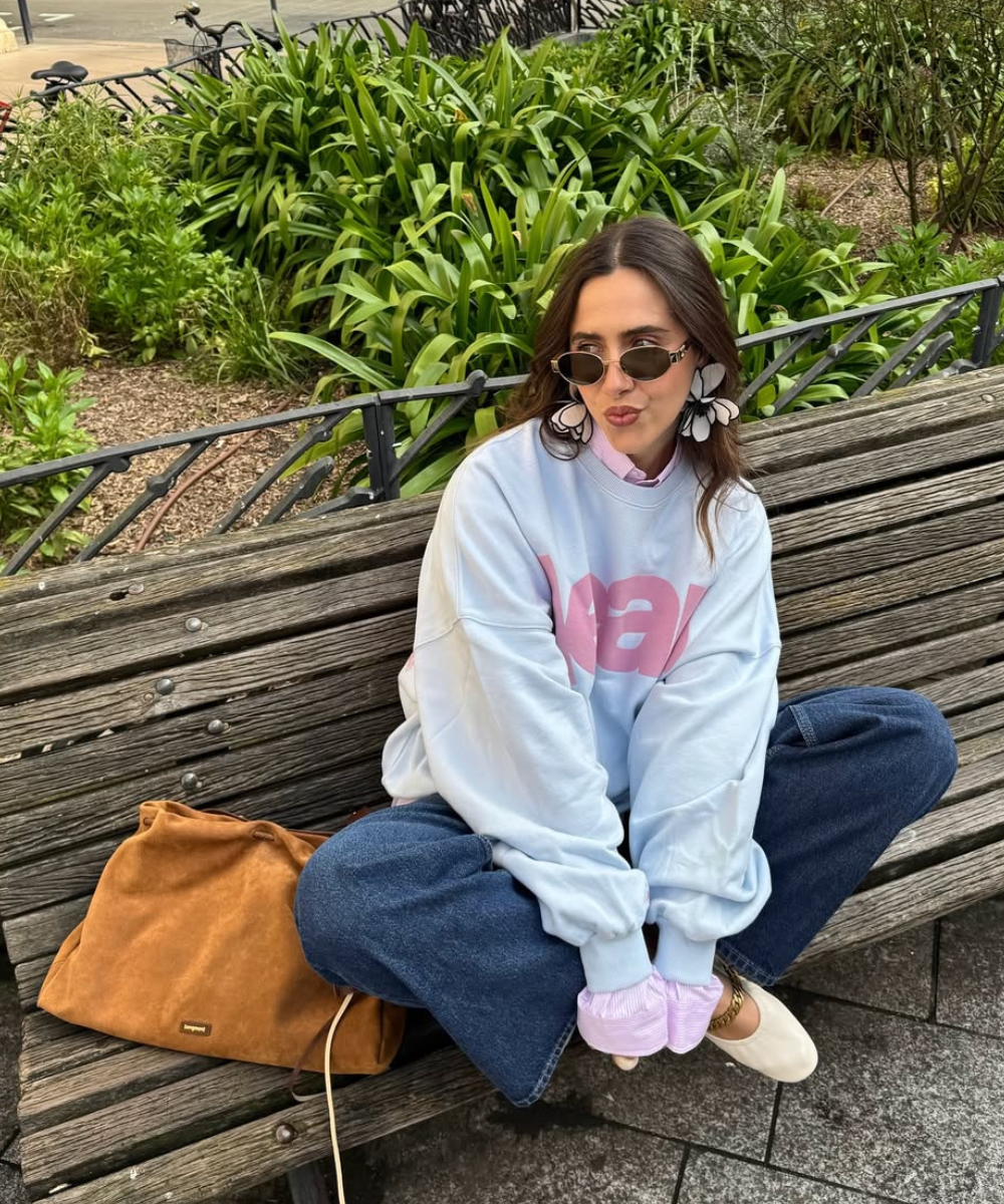 Modelo sentada casualmente no banco usa acessório estiloso com maxi brincos florais em branco e preto.