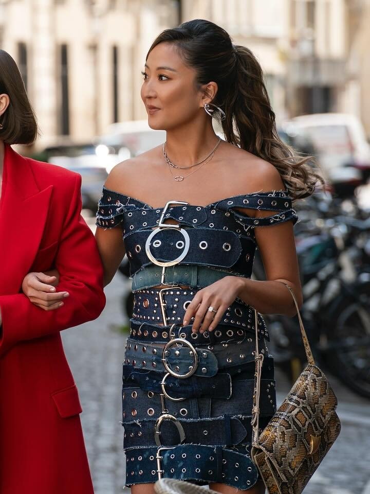 Mulher em postura confiante usa vestido ombro a ombro de jeans com fivelas prateadas e bolsa de couro animal print, clima