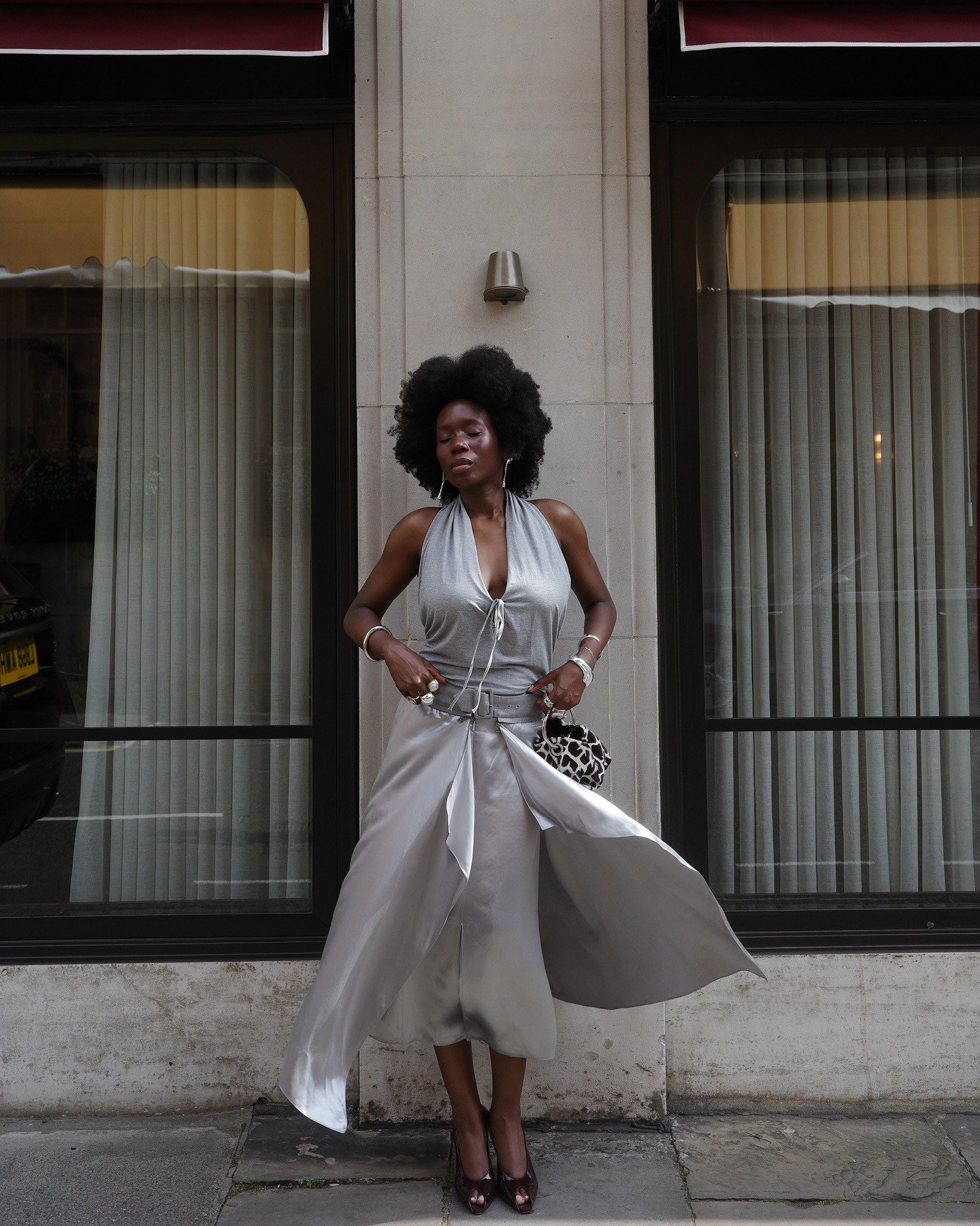 Modelo posa com vestido prata fluido de tecido acetinado e scarpin vinho aberto, realçando elegância e sofisticação nos