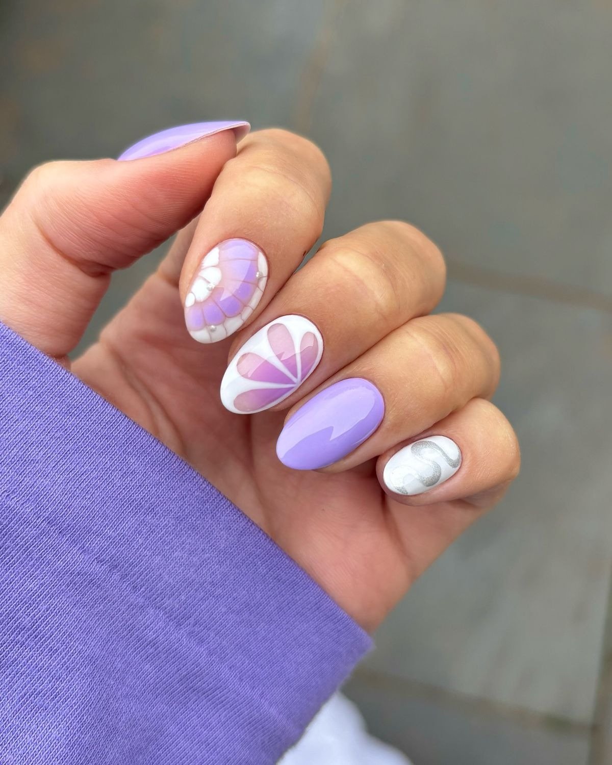 Unhas para Natal 2025 em formato oval com esmalte lilás, detalhes em branco e desenhos delicados que combinam modernidade.