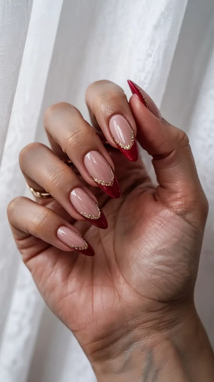 Unhas para Natal 2025 com formato amendoado, base nude, ponta vermelha e delicado contorno dourado.