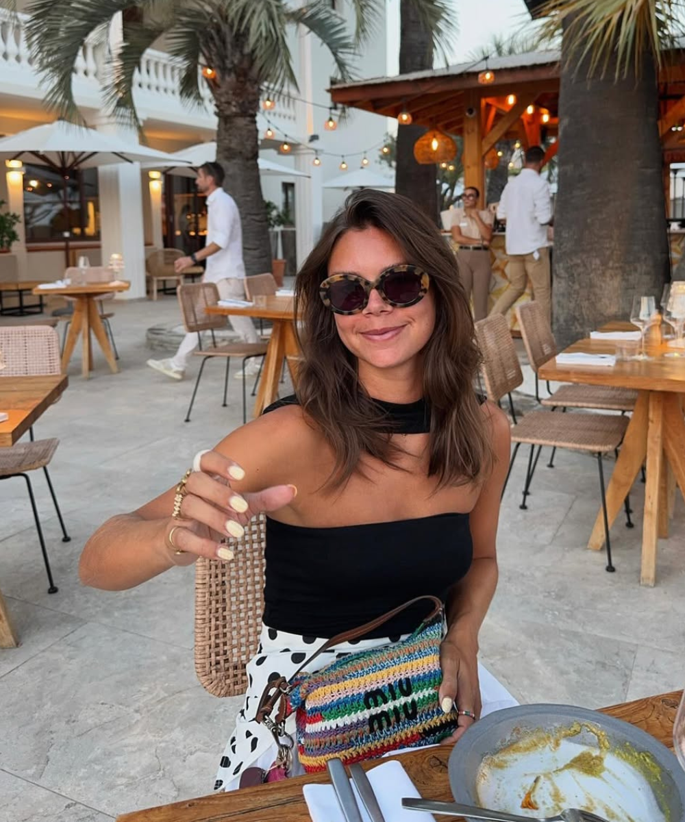 Modelo sorri e posa com óculos tendência 2026 de armação oversized em tartaruga, combinando top preto e saia branca.