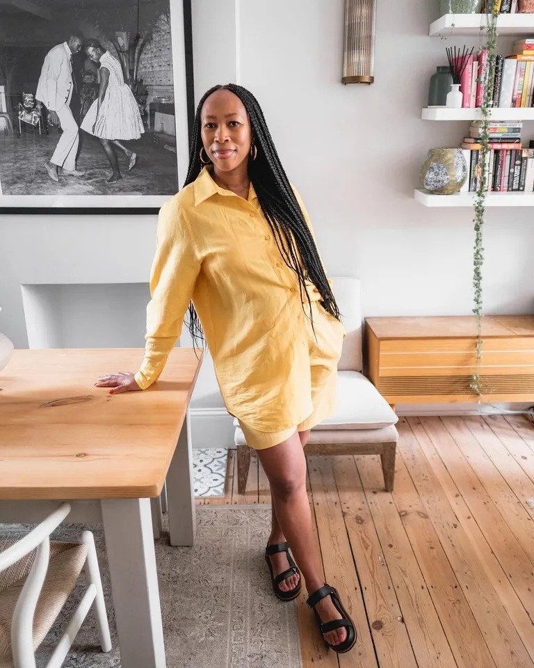 Modelo posa casualmente com camisa e shorts de linho amarelo, combinando conforto e estilo em ambiente aconchegante.