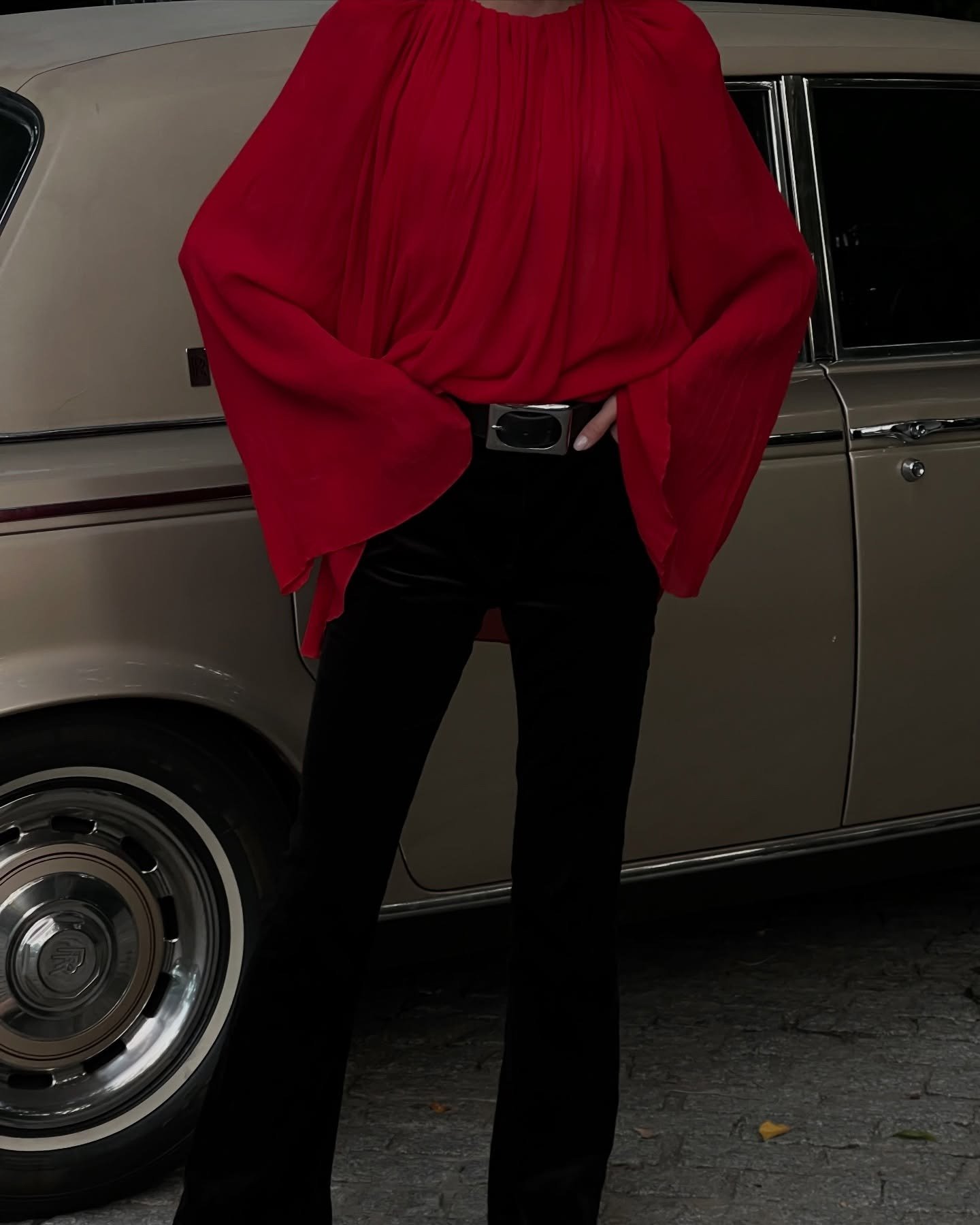 Modelo posa com poncho vermelho de tecido fluido e mangas amplas, combinado a calça preta, em clima sofisticado e urbano.