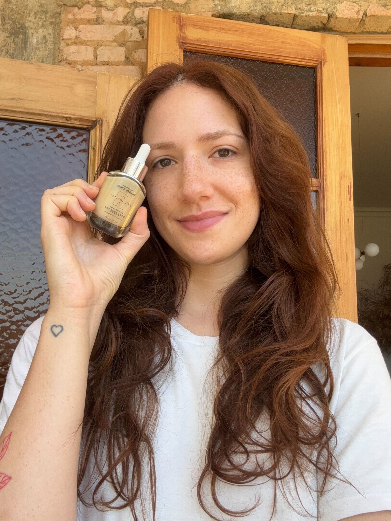 Mulher de cabelos longos e ruivos, camiseta branca, segura sérum facial em vidro com produtos para pele oleosa