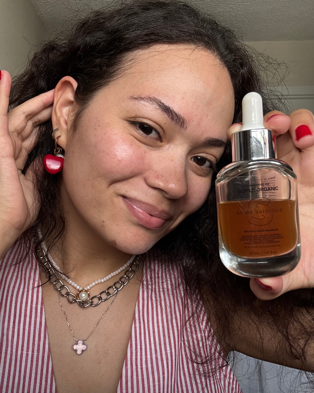 Modelo sorri segurando frasco de ácido salicílico, produtos para pele oleosa veste blusa listrada rosa e branca