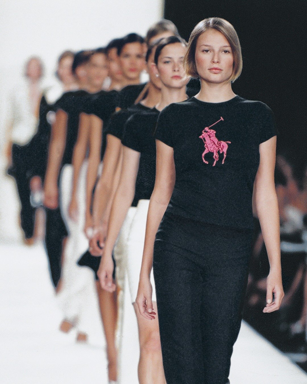 Modelos desfilam com peças básicas Ralph Lauren em preto e branco, destacando camiseta justa com logo rosa.