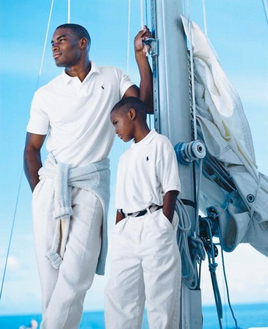 Modelo adulto e criança vestem polos brancas de algodão e calças claras Ralph Lauren, em pose relaxada e elegante no convés