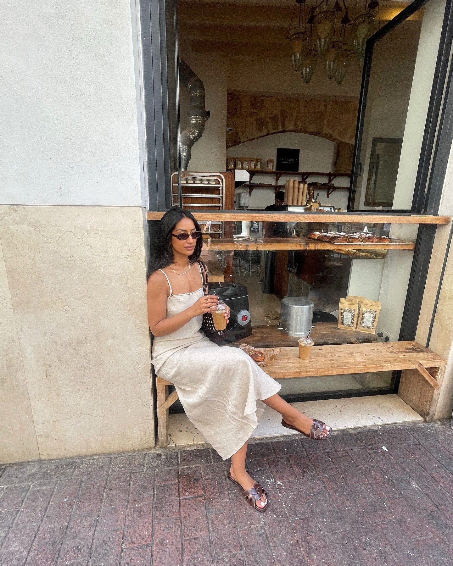 Modelo senta relaxada em vestido longo bege de alças finas e rasteirinha marrom trançada, em clima casual e sofisticado.