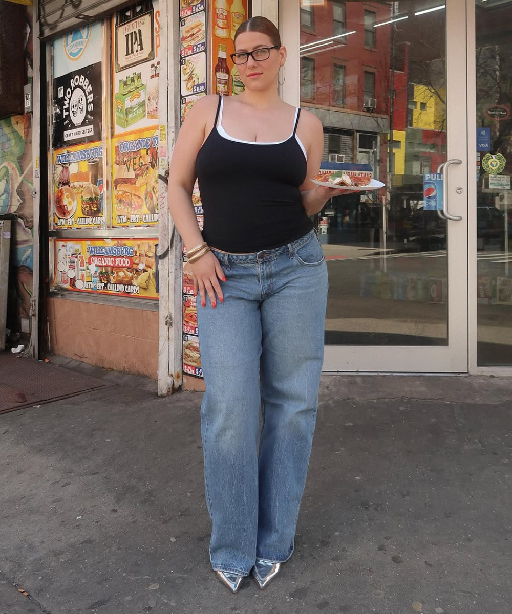 Modelo posa confiante com regata preta de alças finas sobre blusa branca e jeans azul claro de corte reto.