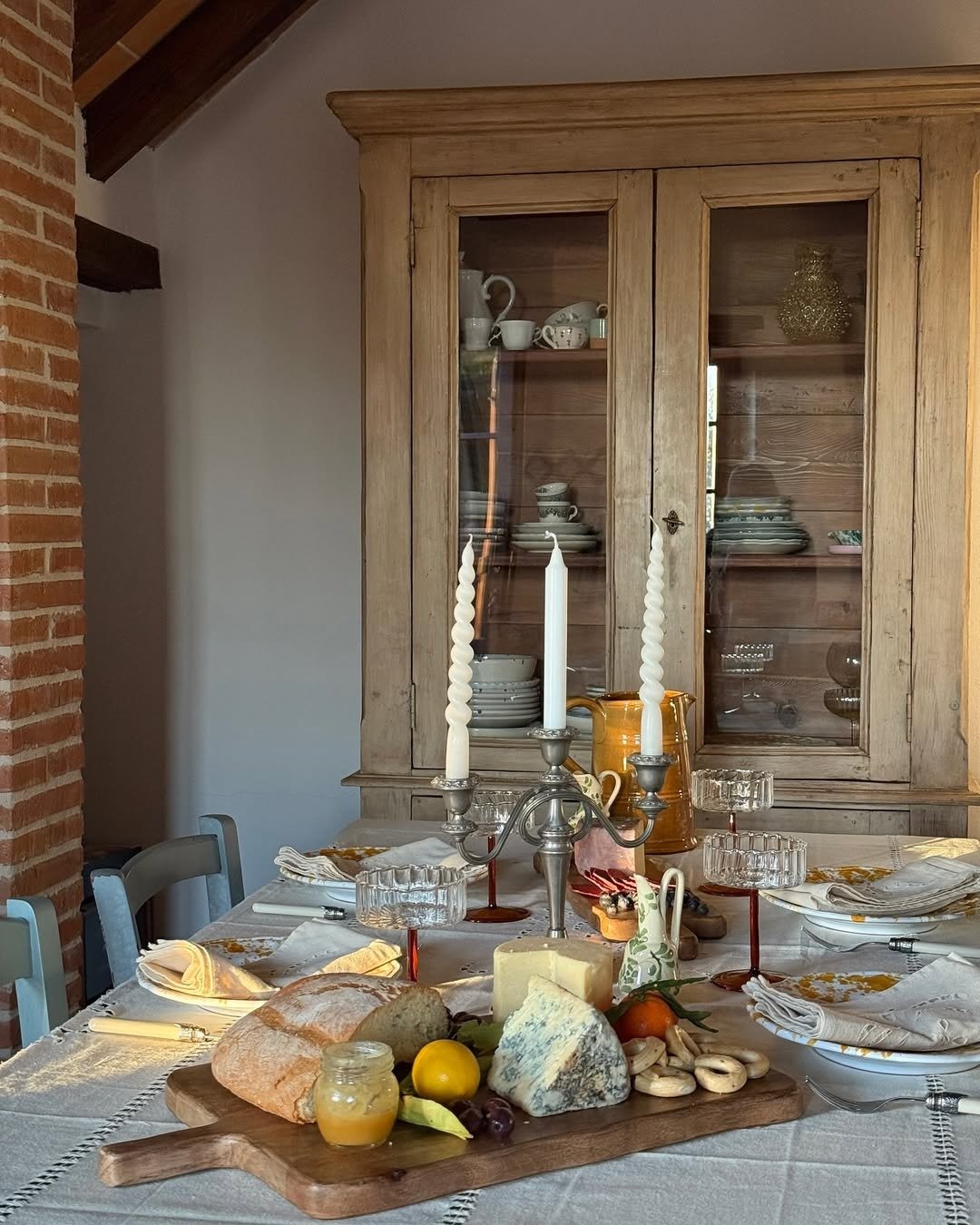 mesa com velas brancas e tábua de madeira com queijos, frutas e pão, ideal para réveillon em casa