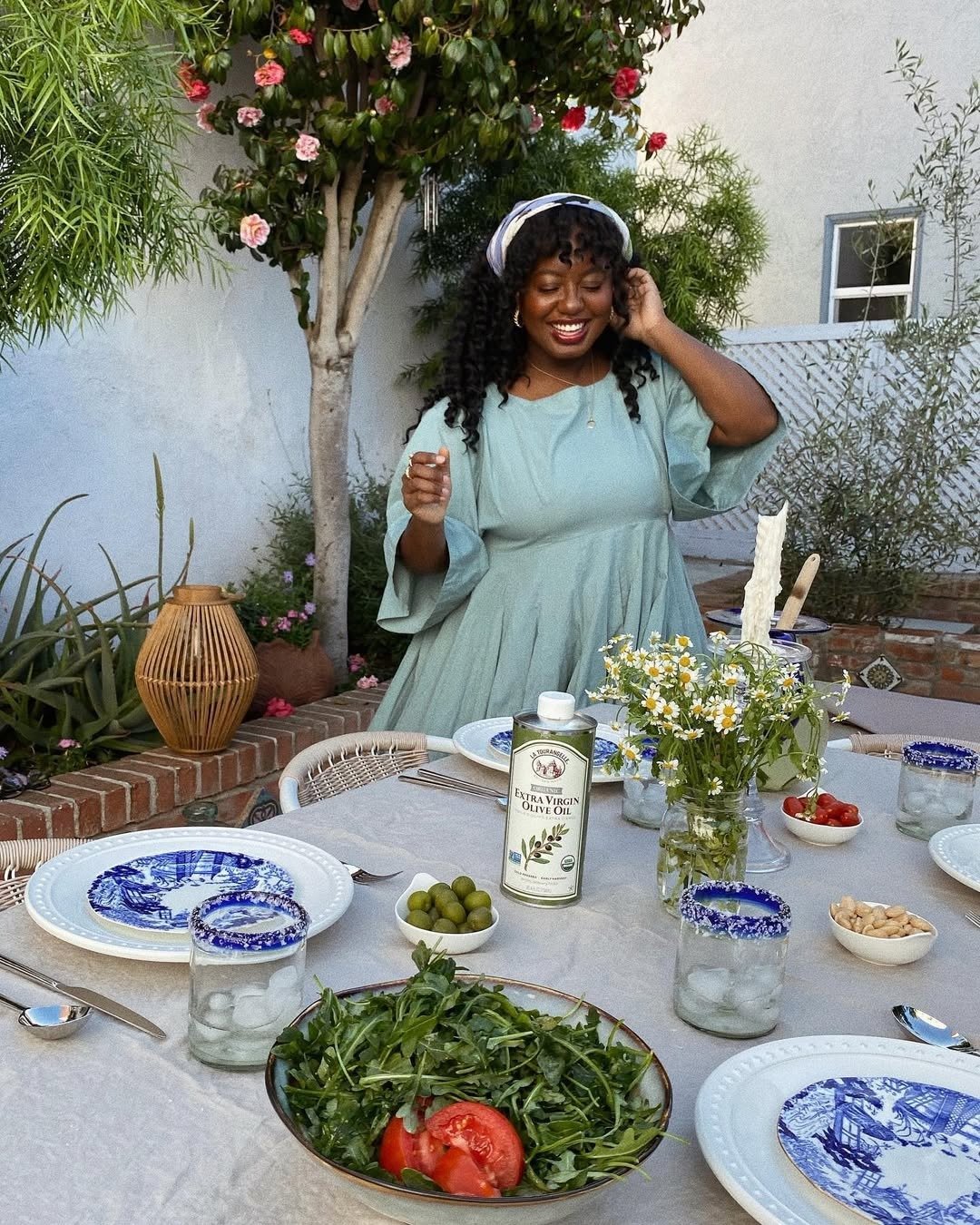 Mulher sorri com vestido verde água fluido e manga ampla, celebrando Réveillon em casa com mesa posta em azul e branco,