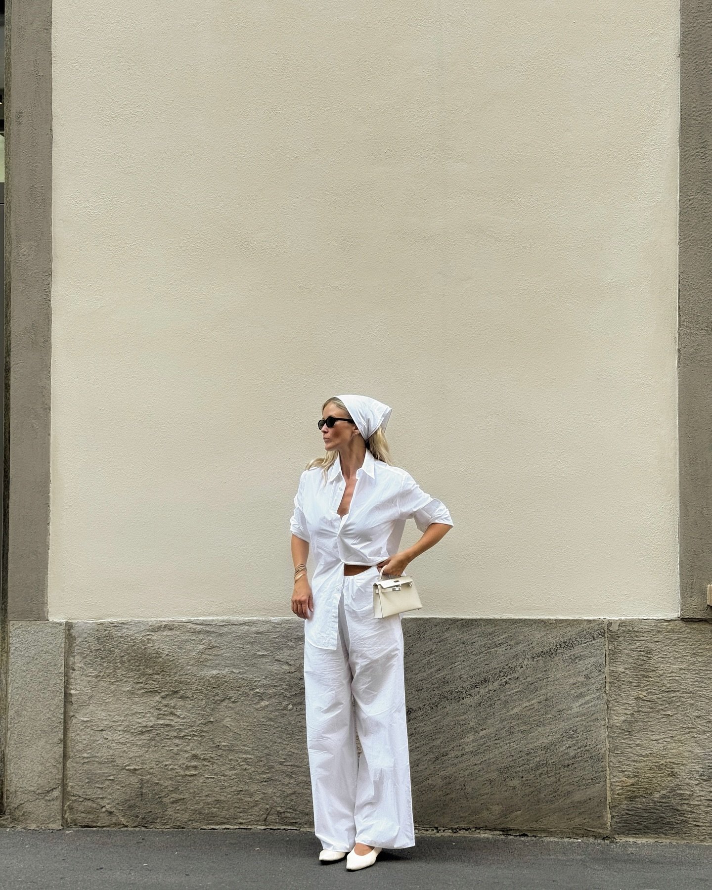 Modelo posa com postura confiante usando sapato clássico e sofisticado branco de bico fino, calça ampla e camisa branca,