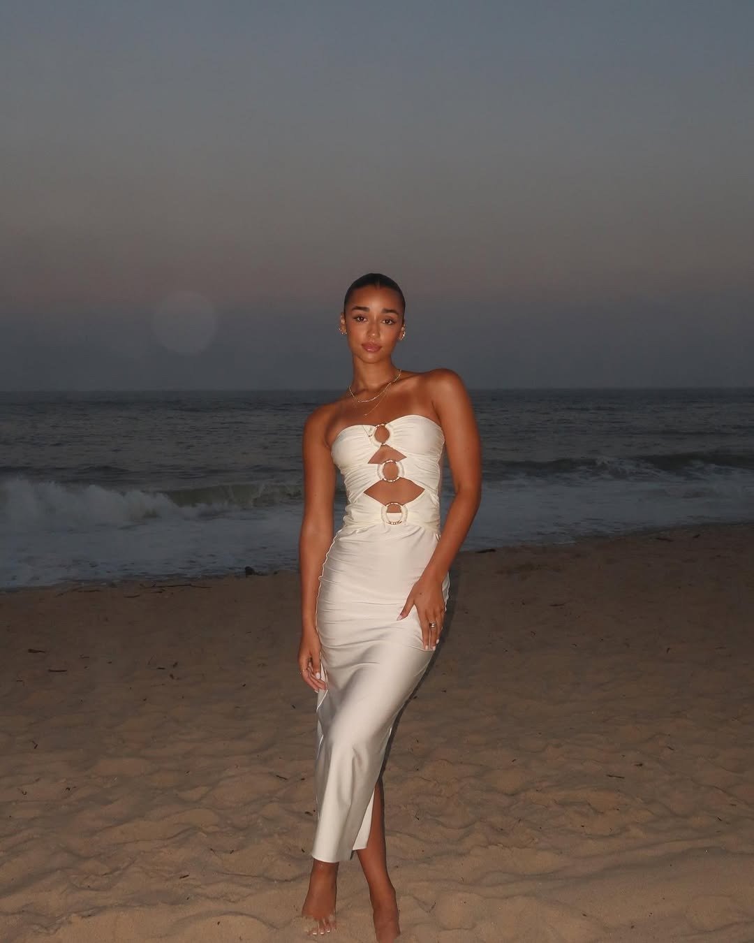 Modelo posa com vestido longo off-white de tecido acetinado e recortes, sapatos confortáveis para festas de fim de ano