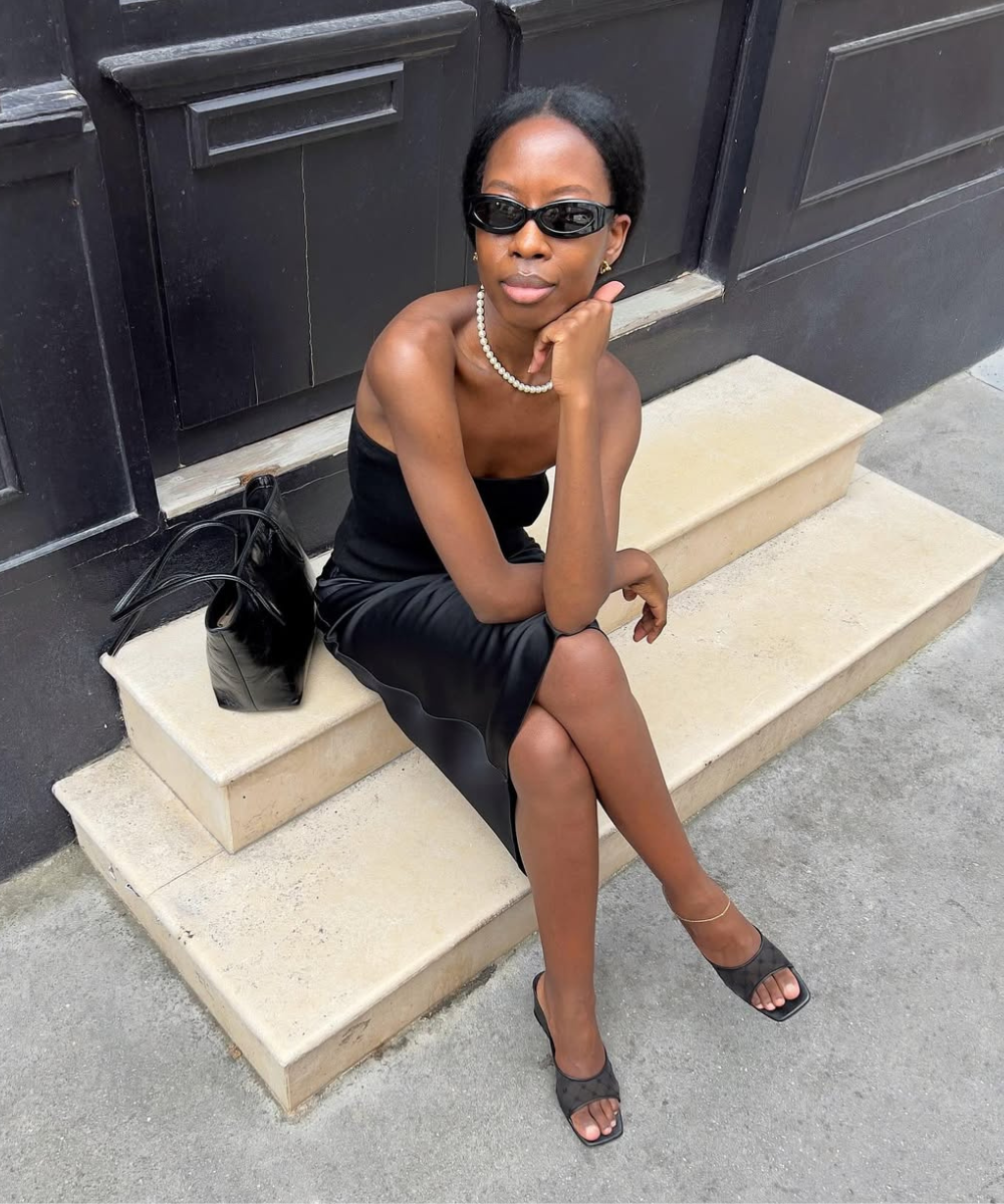 Modelo posa sentada com vestido preto de cetim e sapatos tendência para o verão 2026 em mesh preto com salto baixo.