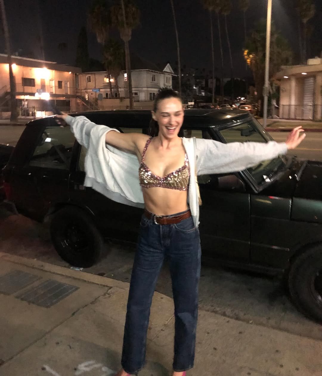 Estilo de Devon Lee Carlson aparece em look com top de paetês dourados, jeans de cintura alta e moletom cinza aberto, em