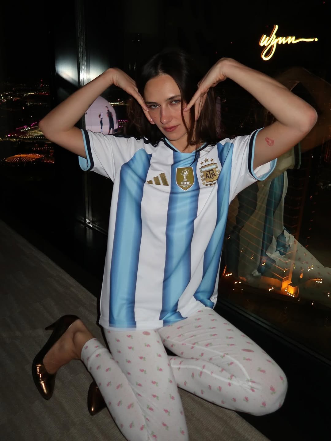 Devon Lee Carlson mistura camiseta de futebol Argentina com legging floral justa e scarpin metálico, posando descontraída e