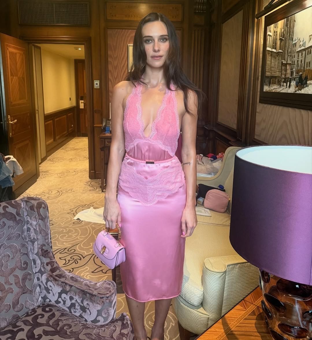 Devon Lee Carlson exibe estilo com vestido rosa de cetim e renda, modelagem ajustada e decote profundo, postura serena e