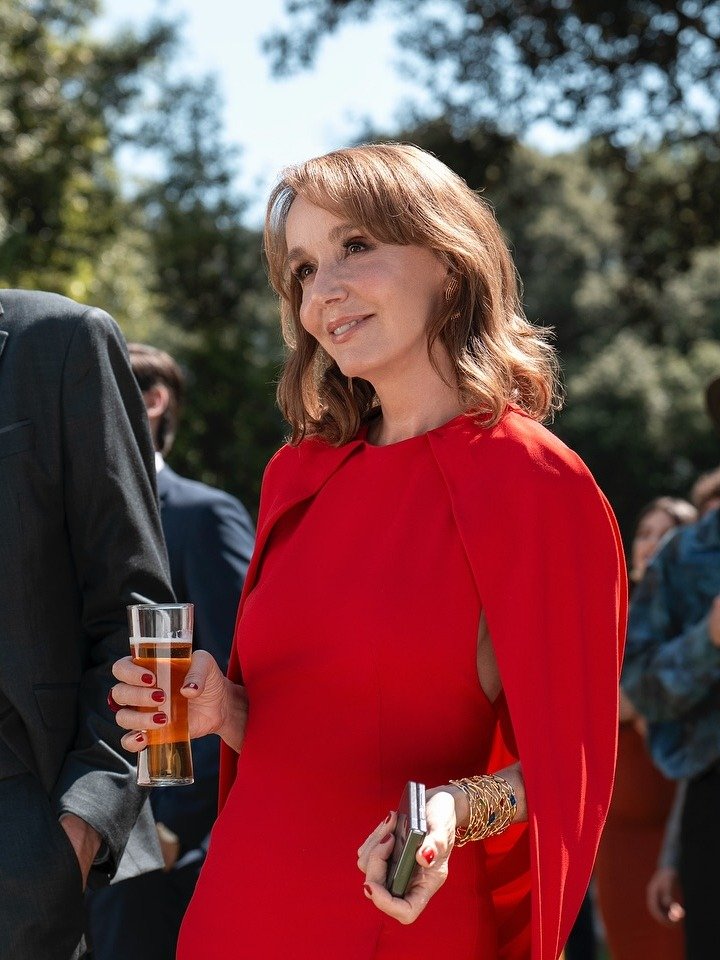 Personagem de Emily em Paris veste vestido vermelho com capa, modelagem ajustada e acessórios dourados, sorrindo