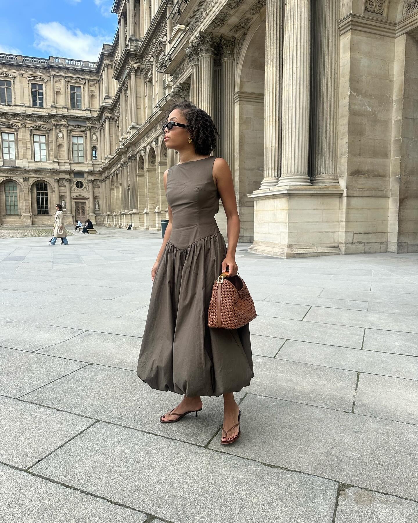 Modelo posa com vestido midi marrom de tecido estruturado e saia ampla, combinando tamanco marrom de tiras finas .