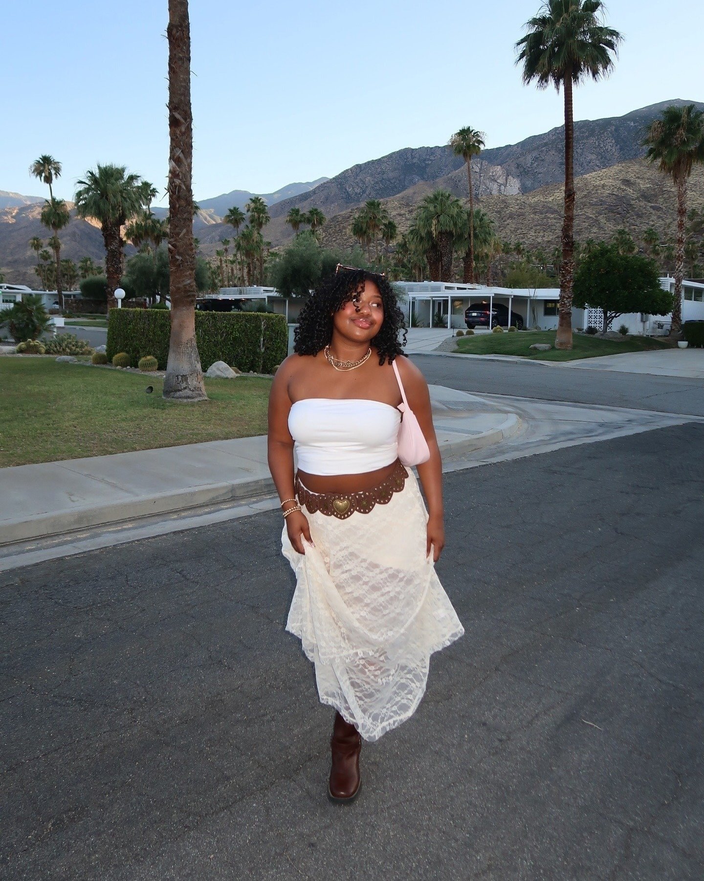 Modelo caminha confiante em look das tendências de moda de 2025 com top branco tomara que caia, saia rendada bege, cinto