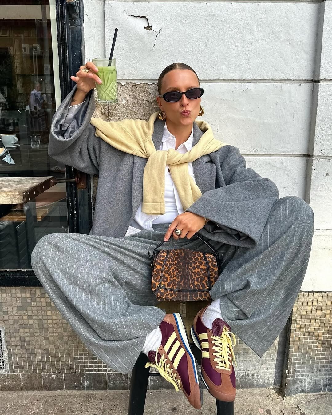 Modelo sentada com postura descontraída exibe tênis tendência da Adidas em tons vinho e amarelo, combinando alfaiataria