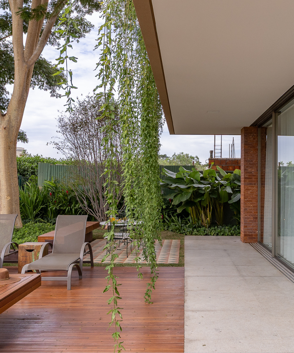 Varanda com piscina exibe parede de tijolinho aparente em tom terroso, deck de madeira e vegetação suspensa, criando