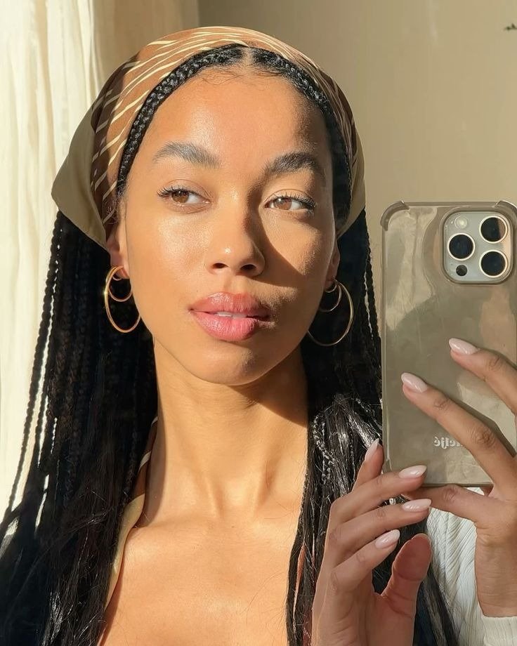 Penteados com trança ganham destaque em fios longos e finos, combinados com lenço marrom estampado e argolas douradas.