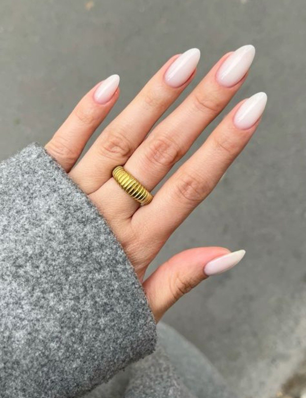 Unhas para Ano Novo em formato amêndoa com esmalte nude perolado, combinando elegância e delicadeza com anel dourado.