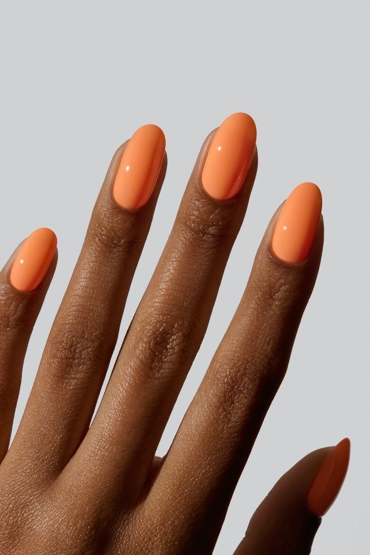 Unhas para Ano Novo com esmalte laranja vibrante, acabamento brilhante e formato oval elegante que destaca a pele morena.