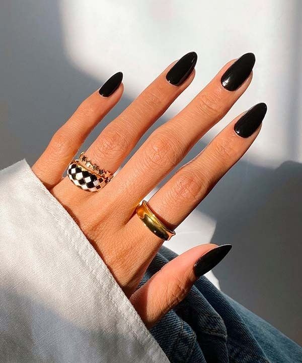 Unhas para Ano Novo em formato amendoado com esmalte preto brilhante, combinadas a anéis dourados e peça xadrez.