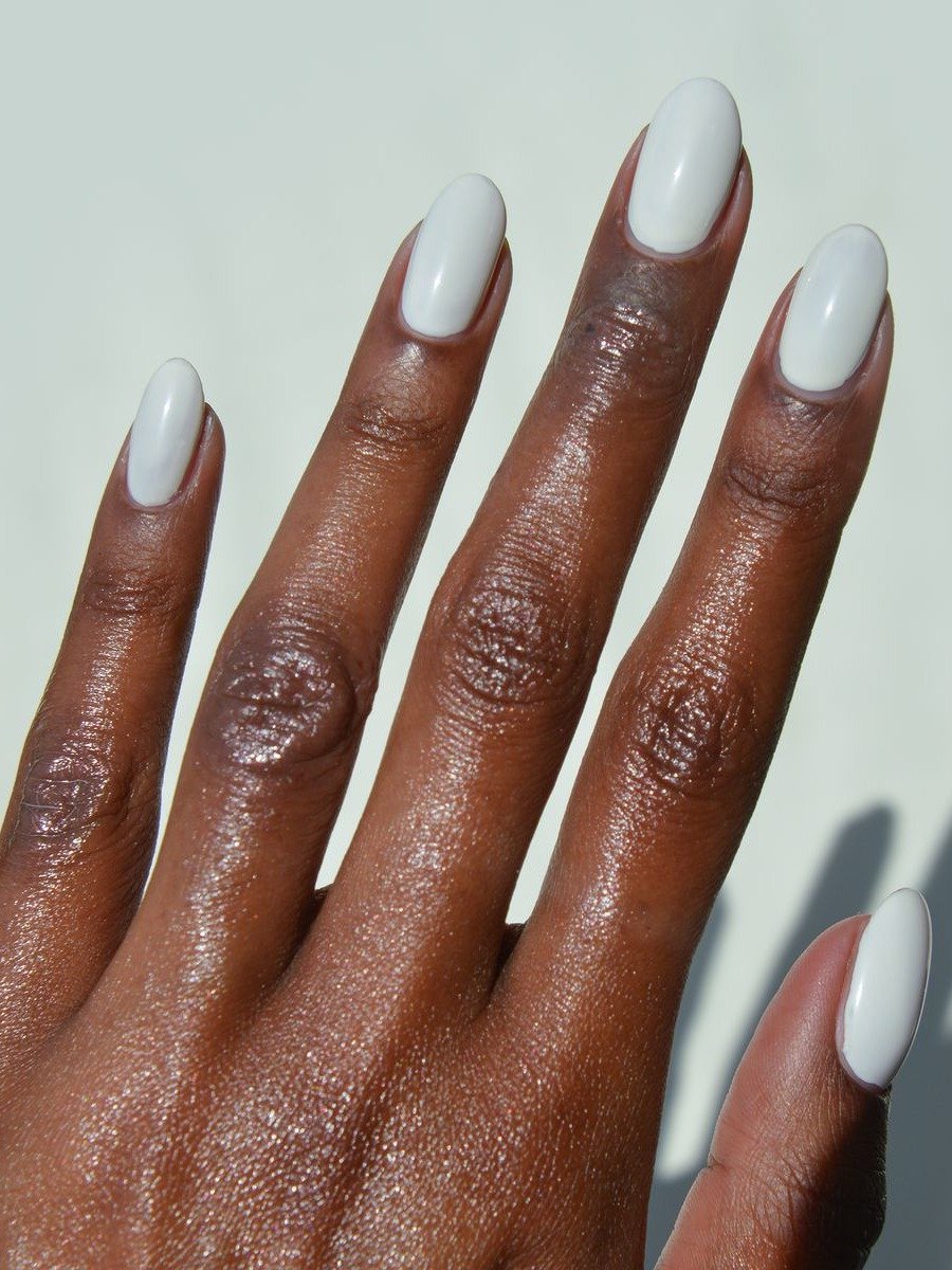 Unhas brancas em formato oval destacam a pele negra com acabamento brilhante, evidenciando cuidado e elegância minimalista.