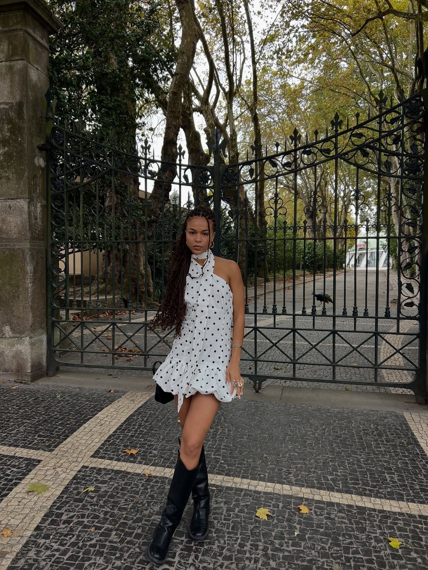 Modelo posa com vestido frente única branco de poás pretos, tecido leve e babados na barra, combinando com botas pretas