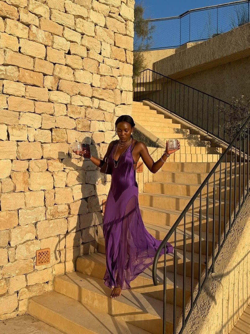 Modelo desce escada com vestido frente única roxo em tecido fluido e transparente, irradiando elegância.