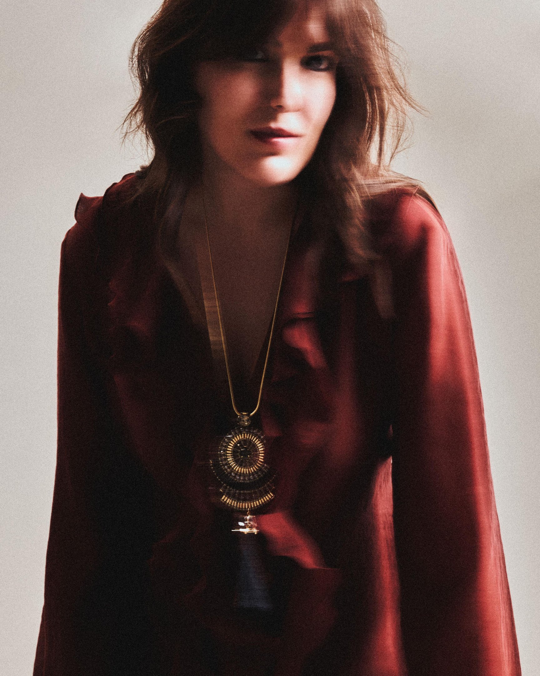 Bia Perotti posa de perfil com expressão serena, usando blusa preta de tecido leve e colar statement com pedras facetadas 