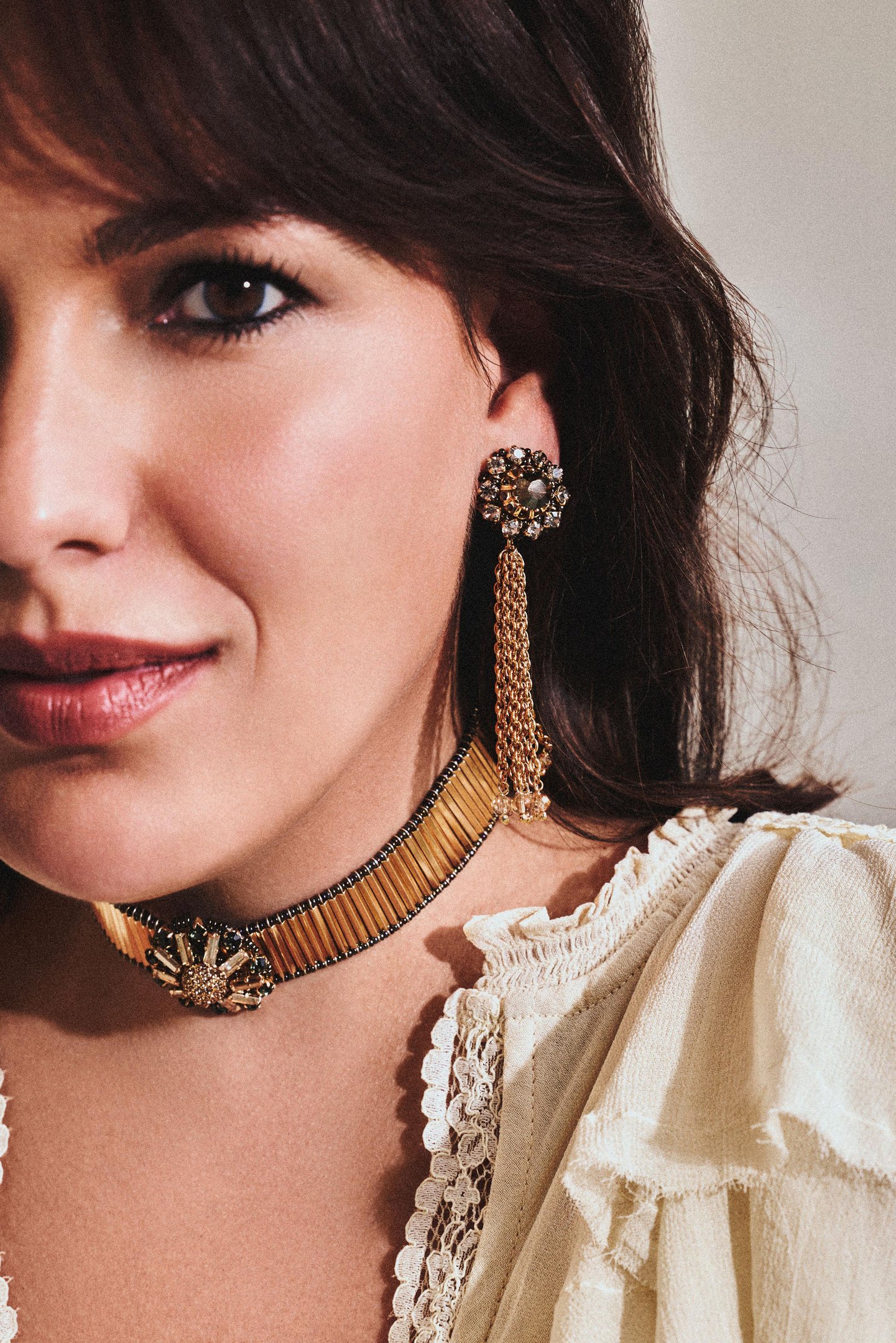 Bia Perotti destaca-se com maxi brinco dourado de correntes, choker detalhada e blusa off-white de renda e babados, em pose