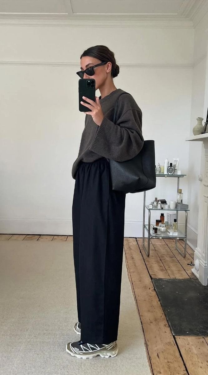 looks com tênis esportivo - Modelo posa de lado com look casual que combina suéter oversized cinza, calça preta de modelagem
