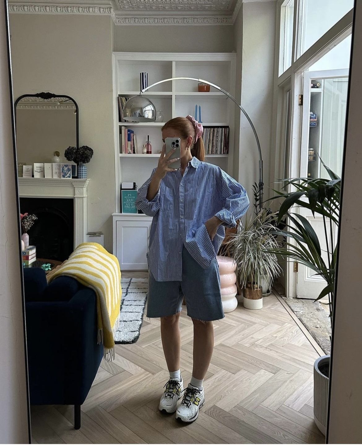 Looks com tênis esportivo - branco e cinza, bermuda jeans ampla e camisa oversized listrada azul, em pose casual e