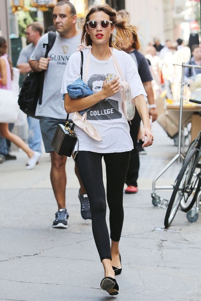 Modelo caminha confiante com calça legging preta justa, camiseta branca oversized e acessórios casuais em ambiente urbano.