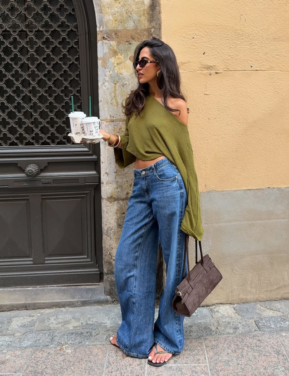 Batas femininas em malha verde oliva com modelagem ampla e ombro único, combinadas com jeans largos e acessórios casuais.