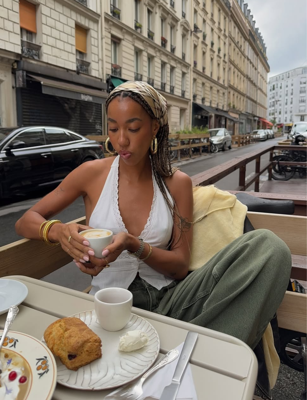 Modelo senta em café ao ar livre usando blusa feminina da moda branca com decote em V e detalhes rendados.