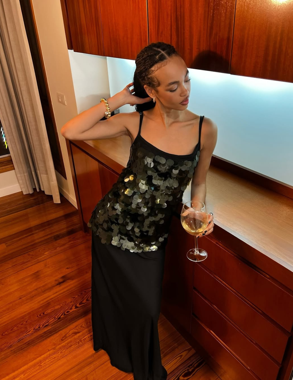 Blusas femininas da moda ganham brilho com modelagem regata e paetês pretos, enquanto a modelo posa elegante.