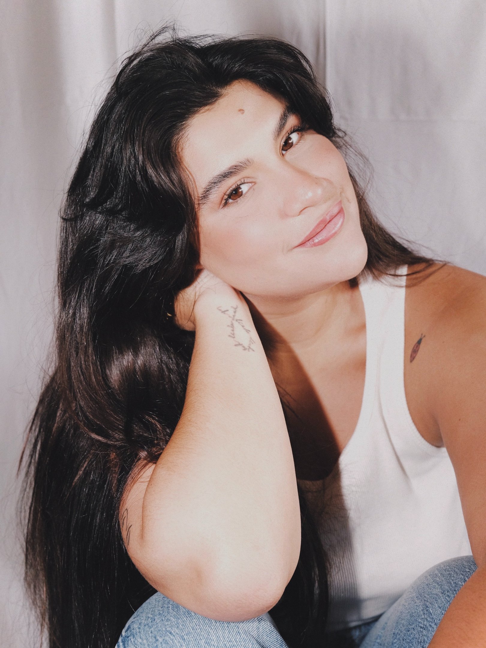 Mulher com regata branca e jeans claros sorri suavemente, após reflexão sobre bullying na infância