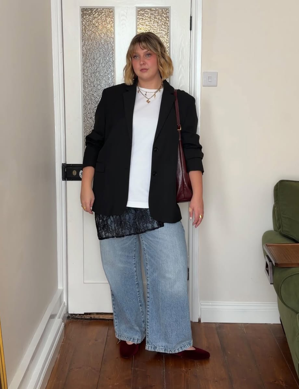 Modelo posa com calça jeans boyfriend azul clara de modelagem ampla, combinada a blazer preto, camiseta branca e bolsa.