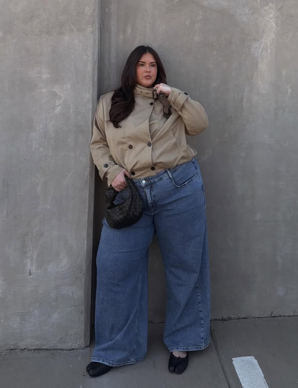 Modelo posa encostada com calça jeans boyfriend azul de lavagem média e modelagem ampla, combinada a jaqueta bege cropped.