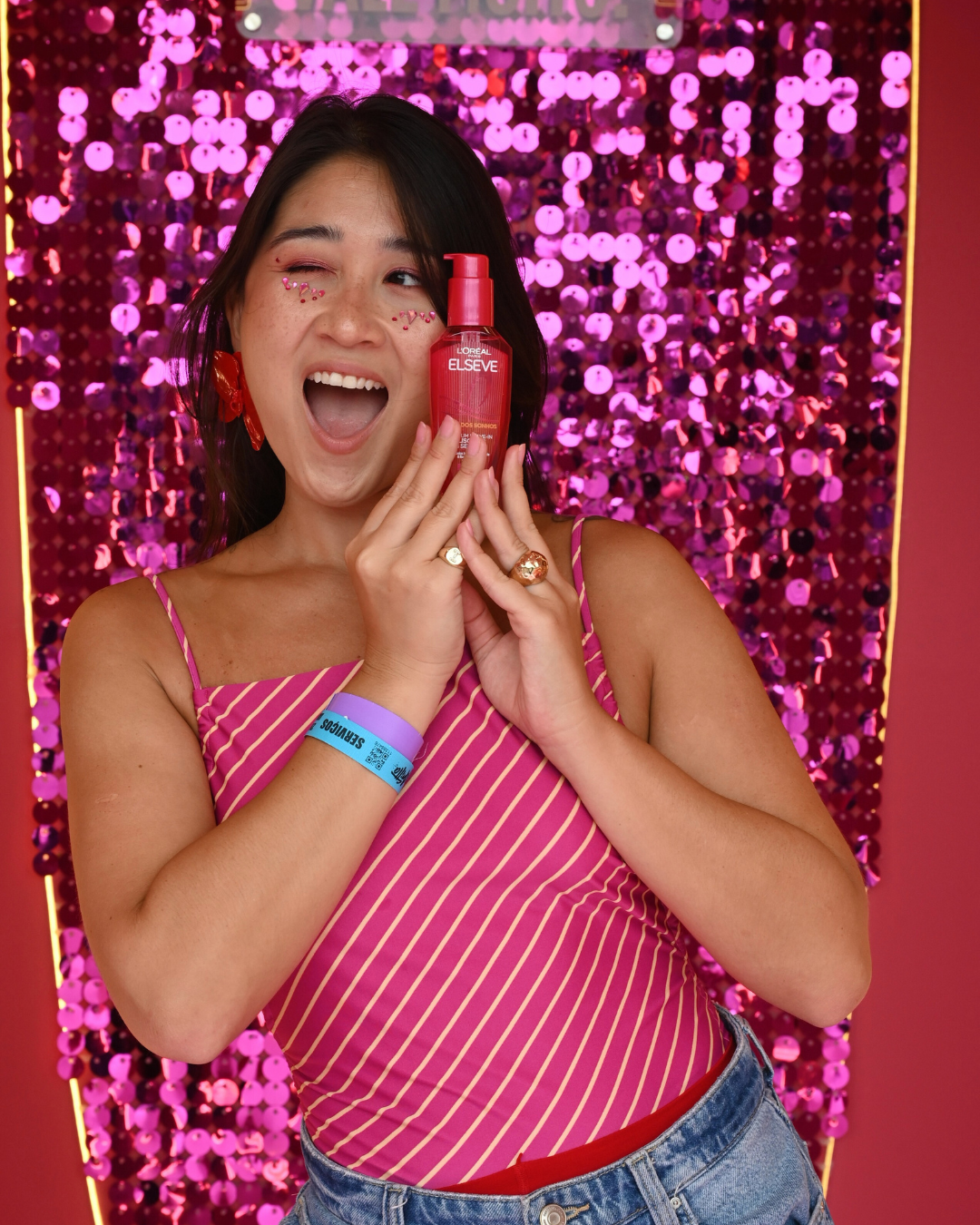 Carnaval 2026 traz blusa rosa com listras finas, acessórios vermelhos e jeans, com brilho e alegria em pose animada