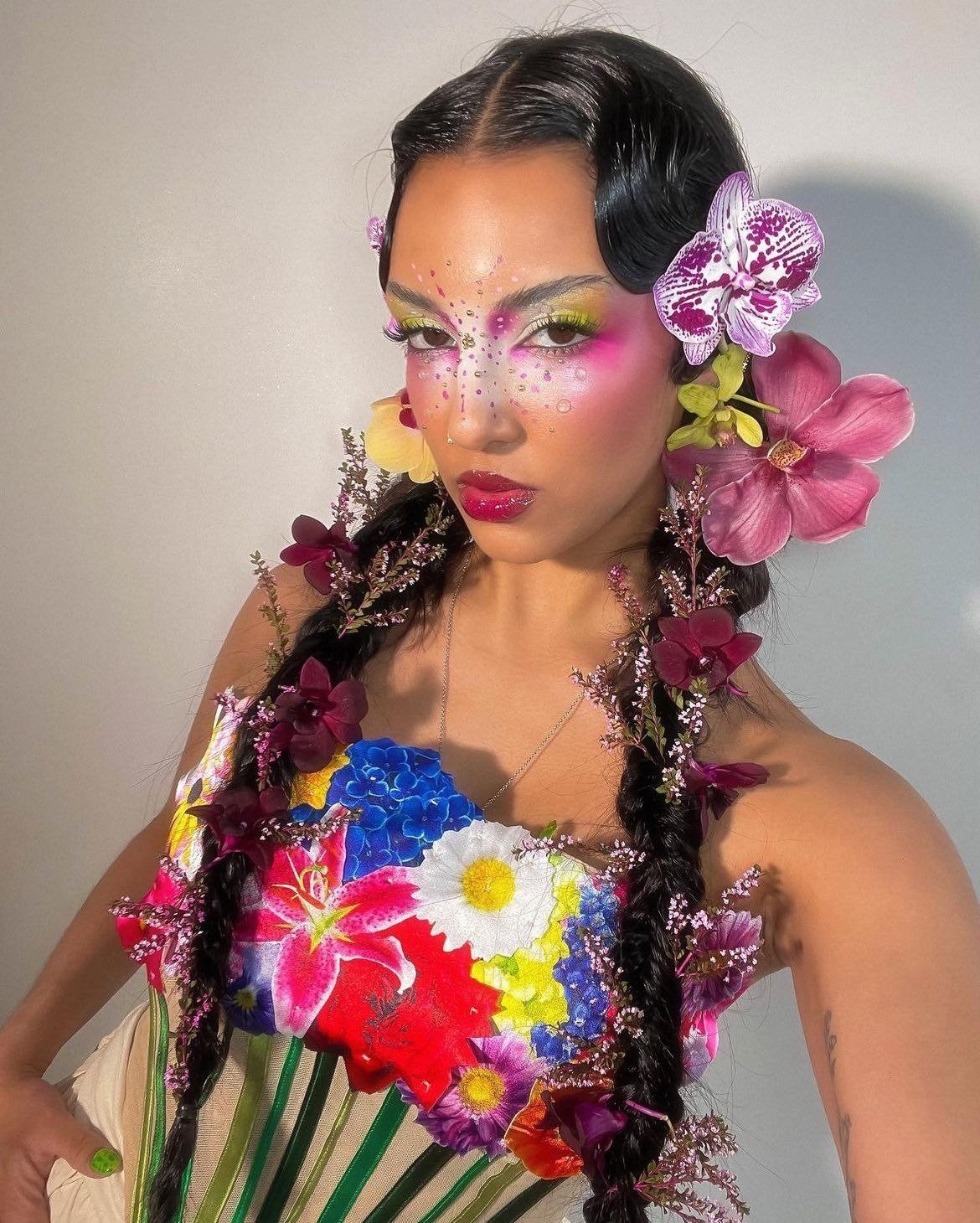 Modelo posa com acessórios de Carnaval florais vibrantes em tranças, maquiagem colorida e vestido estampado